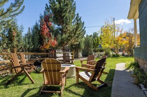 An outdoor seating area with wooden chairs and tables, surrounded by trees with autumn foliage.