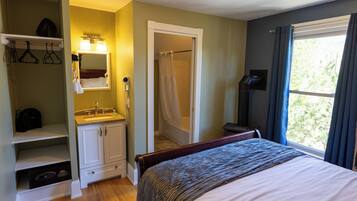Une chambre à coucher comprenant un lit, un dressing, une salle de bain avec douche et une fenêtre avec des rideaux.