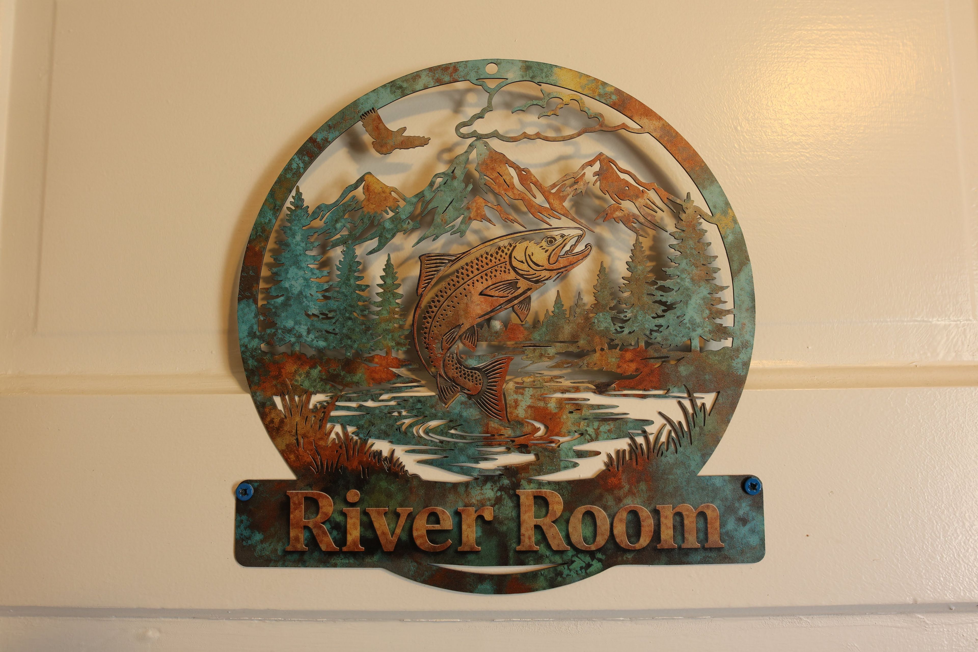 Ein Metallschild mit einem Fisch und Bäumen, beschriftet mit 'River Room'.