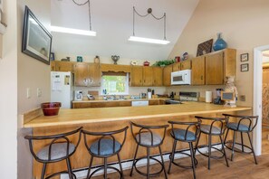 Une cuisine avec des meubles en bois, un grand îlot central doté de tabourets, un four à micro-ondes et une fenêtre donnant sur un espace verdoyant.