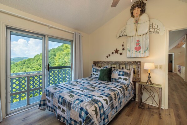 A bedroom with a large bed, a view of the outdoors through a sliding door, and a decorative wall piece. - Mountain Top Haven: Smoky Mountain Views, Hot Springs Spa & Spacious Yard (Whittier)