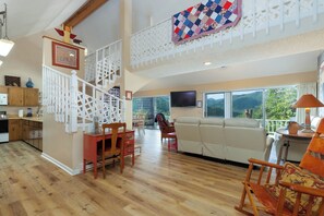 A spacious living area with a high ceiling, a staircase with a decorative railing, a large window with a view of the outdoors, and a television mounted on the wall. - Mountain Top Haven: Smoky Mountain Views, Hot Springs Spa & Spacious Yard (Whittier)