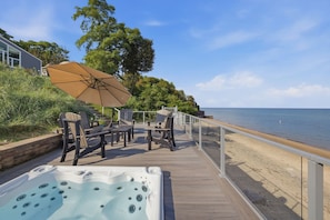 Une terrasse en bois avec coin salon extérieur, un jacuzzi et vue sur la plage.