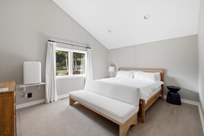 Un dormitorio con cama, banco, mesita de noche, lámpara y ventana con cortinas.