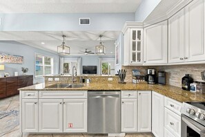 Una cocina moderna con armarios blancos, encimeras de granito y electrodomésticos de acero inoxidable, además de una isla central.