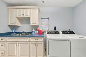 A laundry room with a washing machine, dryer, sink, cabinets, and a window with blinds. - Be A Nomad | 3BR 3BA Townhouse | 2 Blocks to Jacksonville Beach | Sleeps 6 (Jacksonville Beach)