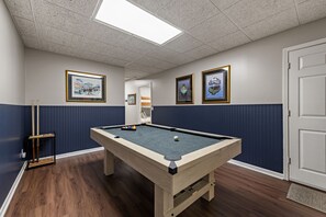 A pool table with a blue felt surface, wooden legs, and a light-colored border. There are two framed artworks on the wall, a door, and a wooden bench with pool cues. - Happy Retreat at Lake Nottely w/kayaks, dock, hot tub, pool table - pets ok! (Blairsville)