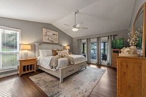 A bedroom with a bed, nightstands, a ceiling fan, a large window, and a view of the outdoors. - Happy Retreat at Lake Nottely w/kayaks, dock, hot tub, pool table - pets ok! (Blairsville)