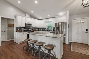 A modern kitchen with white cabinetry, a stainless steel refrigerator, a marble island with stools, and a black countertop. - Happy Retreat at Lake Nottely w/kayaks, dock, hot tub, pool table - pets ok! (Blairsville)