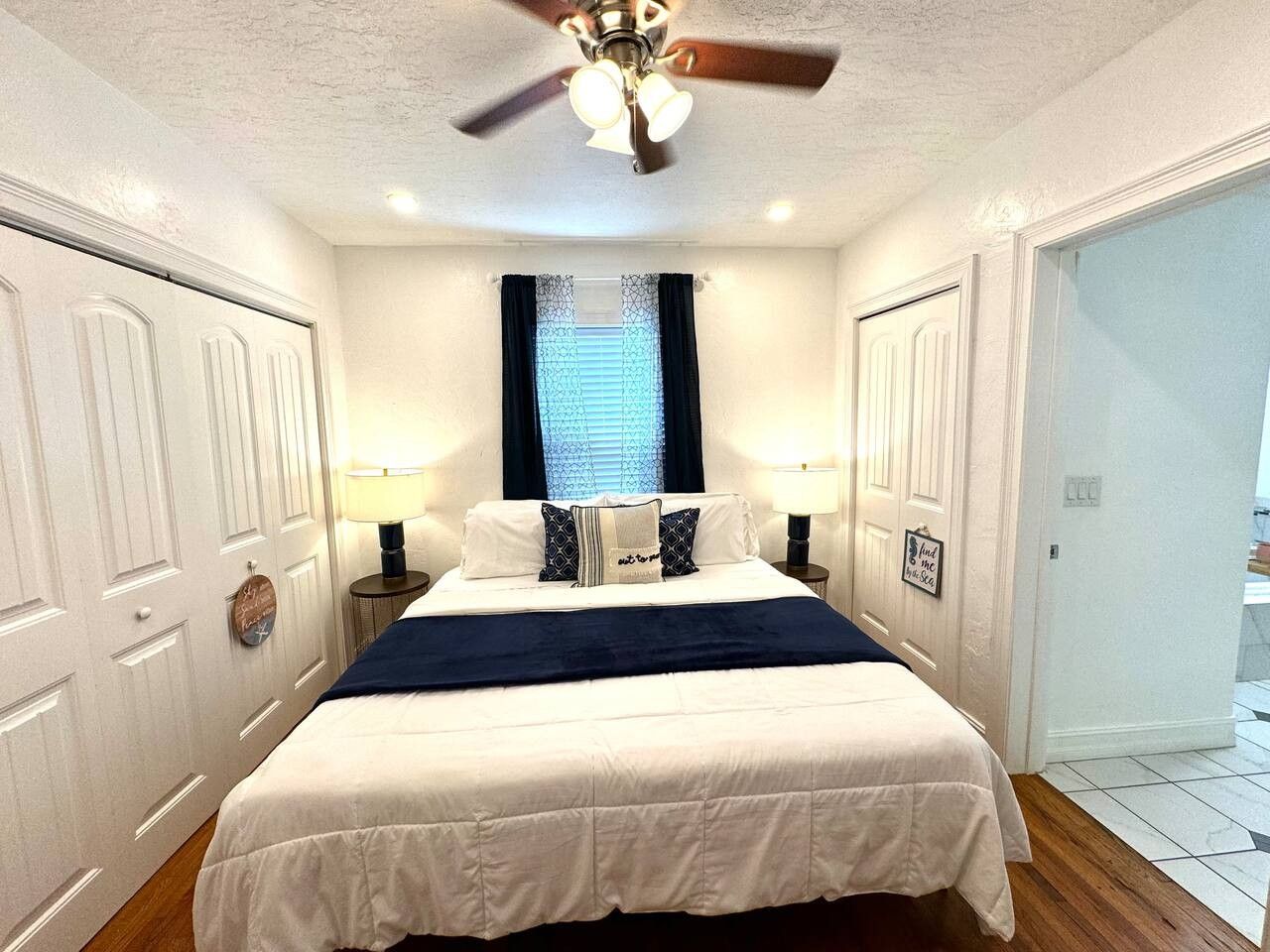 A bedroom with a bed, two bedside tables, a ceiling fan, and a window with curtains.