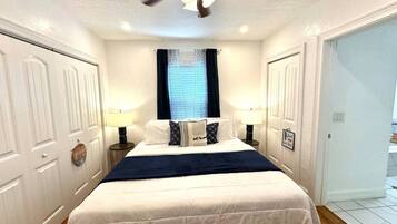 A bedroom with a bed, two bedside tables, a ceiling fan, and a window with curtains.