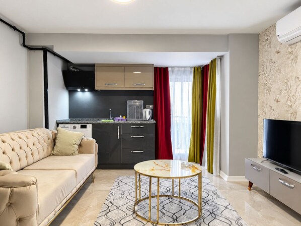 Una sala de estar moderna con un sofá, una mesa de centro, un televisor de pantalla plana y una cocina con armarios y un hervidor.
