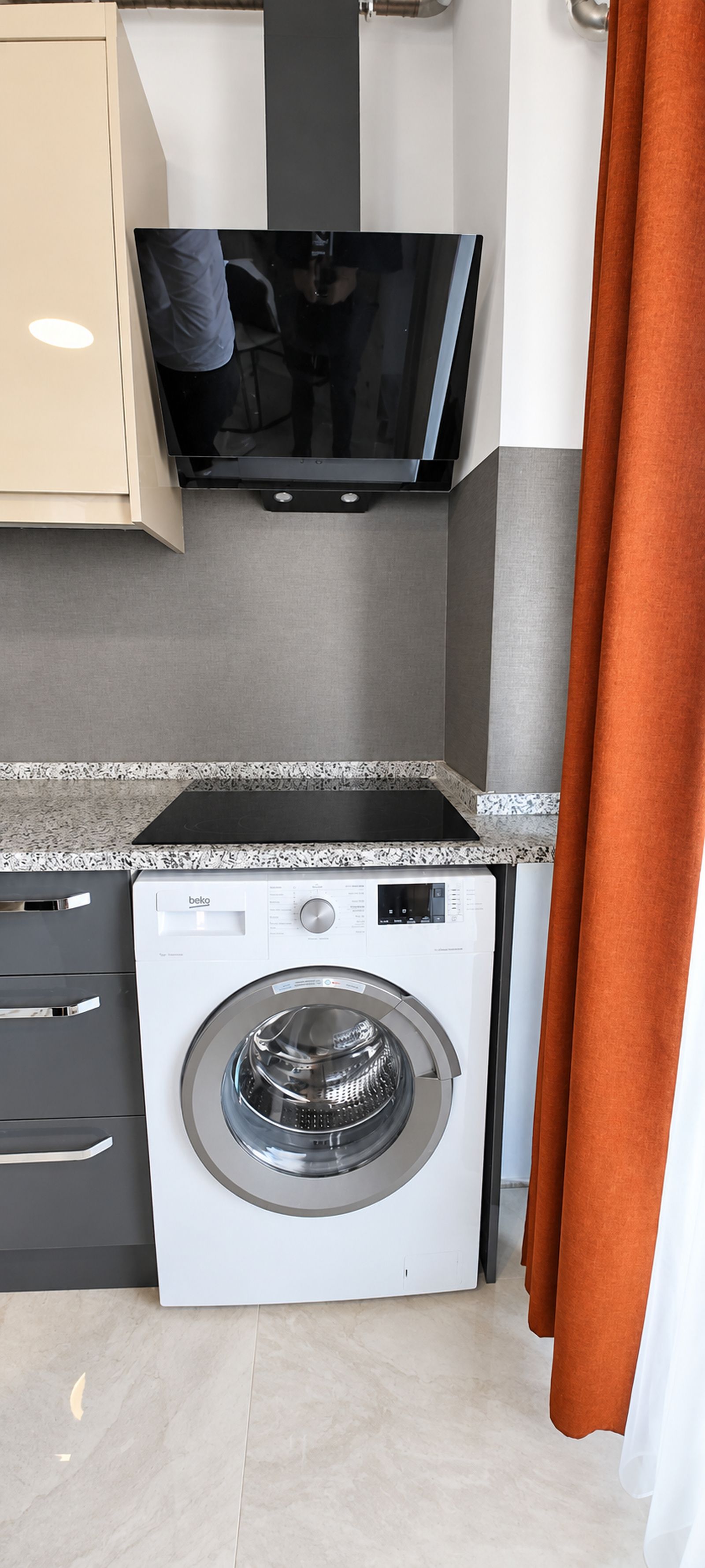 A compact kitchen with a washing machine, a built-in oven, and a flat-screen TV.