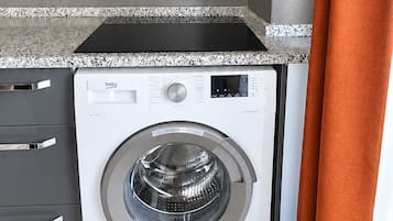 A compact kitchen with a washing machine, a built-in oven, and a flat-screen TV.