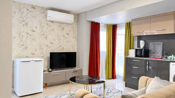 A compact living space with a kitchenette, a flat-screen TV, a refrigerator, and a sofa.