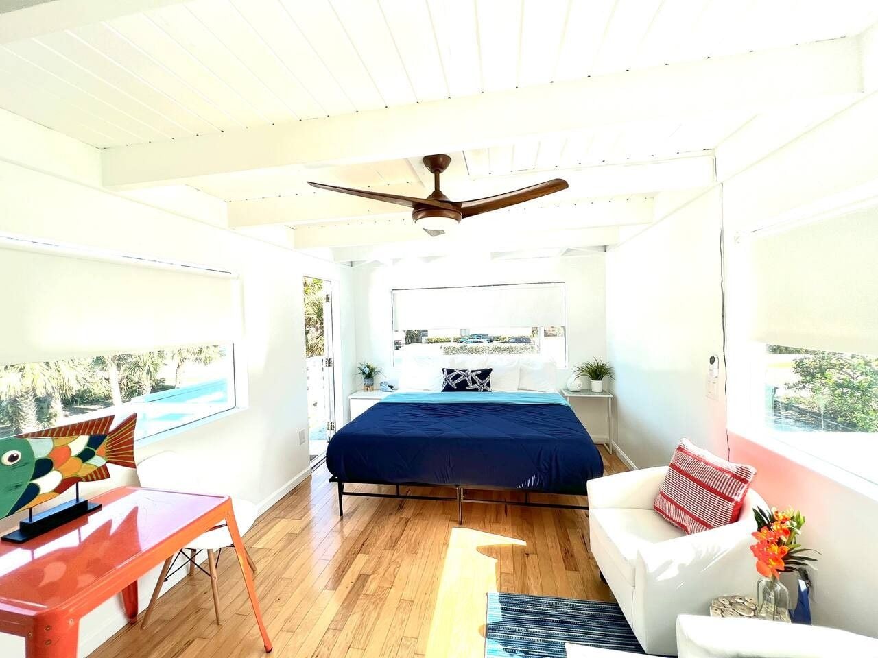 A modern bedroom with a bed, a desk, a chair, and a ceiling fan.
