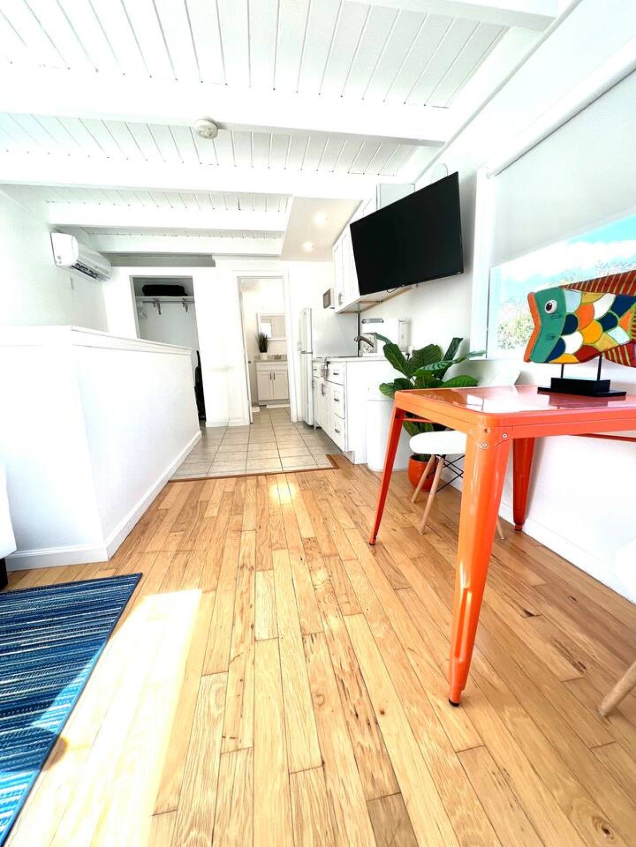 A modern kitchen with a flat-screen TV, wooden flooring, and a bright ceiling.