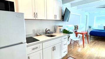 Una cocina moderna con armarios blancos, un microondas integrado y un lavamanos. Hay una zona de comedor con una mesa y sillas, y un televisor montado en la pared.