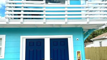 A two-story building with a balcony, two blue doors, and a small window.
