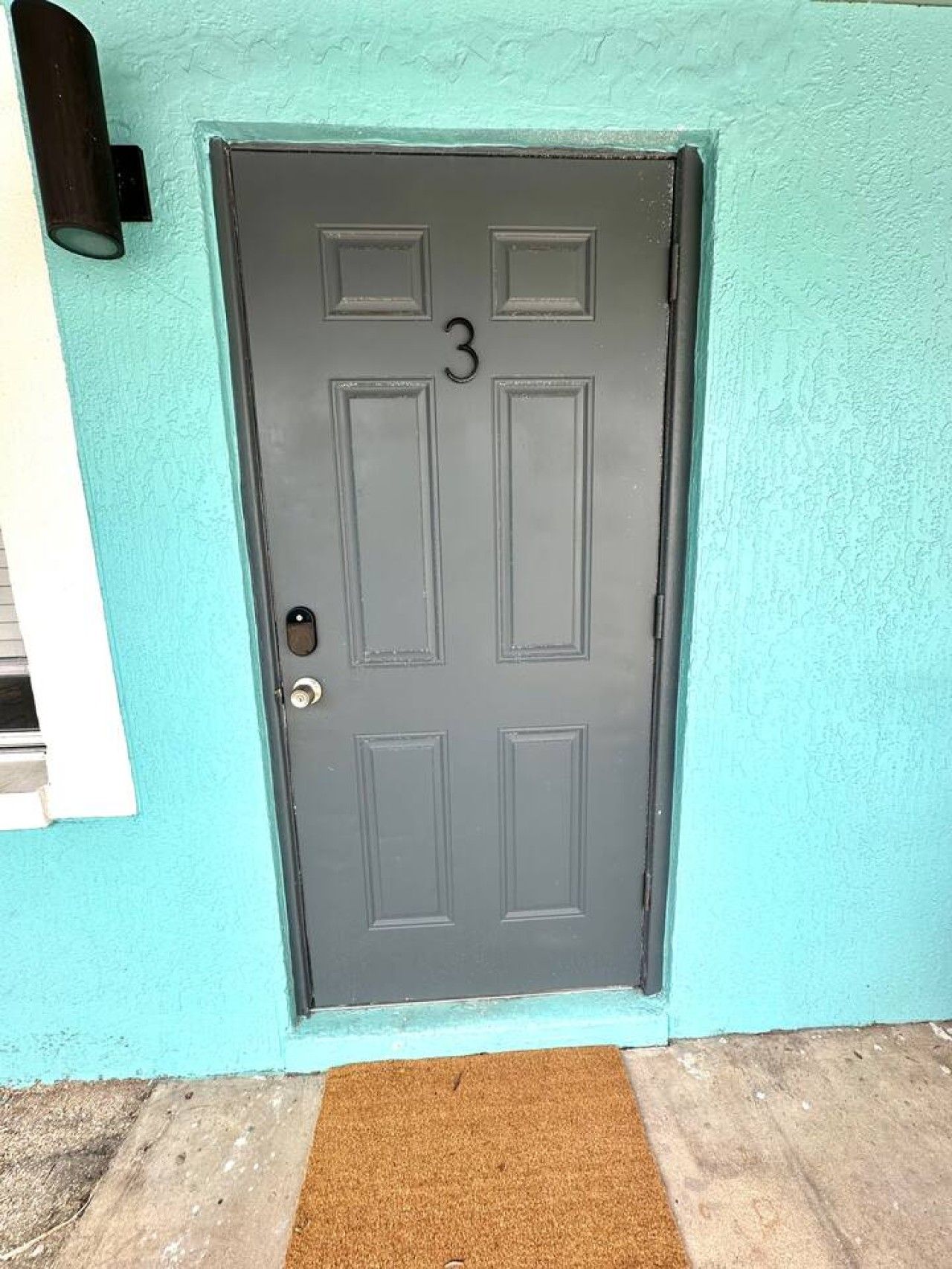 A dark grey door with the number 3, a doormat, and a light blue wall.