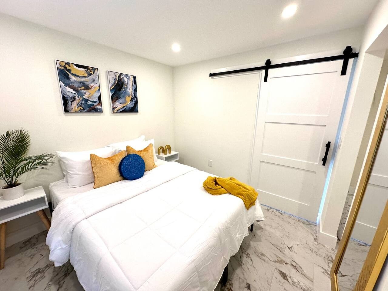 Un dormitorio con cama, mesitas de noche, una planta en maceta, una obra de arte en la pared y una puerta corredera.