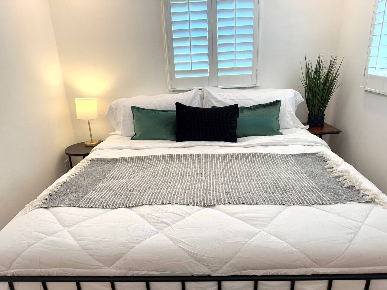 A bed with a white quilted mattress, a grey and white striped throw, and two green pillows.