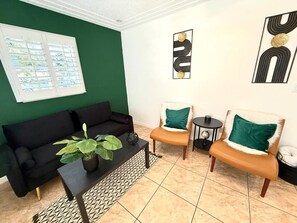 Ein Wohnzimmer mit einer schwarzen Couch, zwei Sesseln, einem Couchtisch mit einer Pflanze und Kunstwerken an den Wänden.