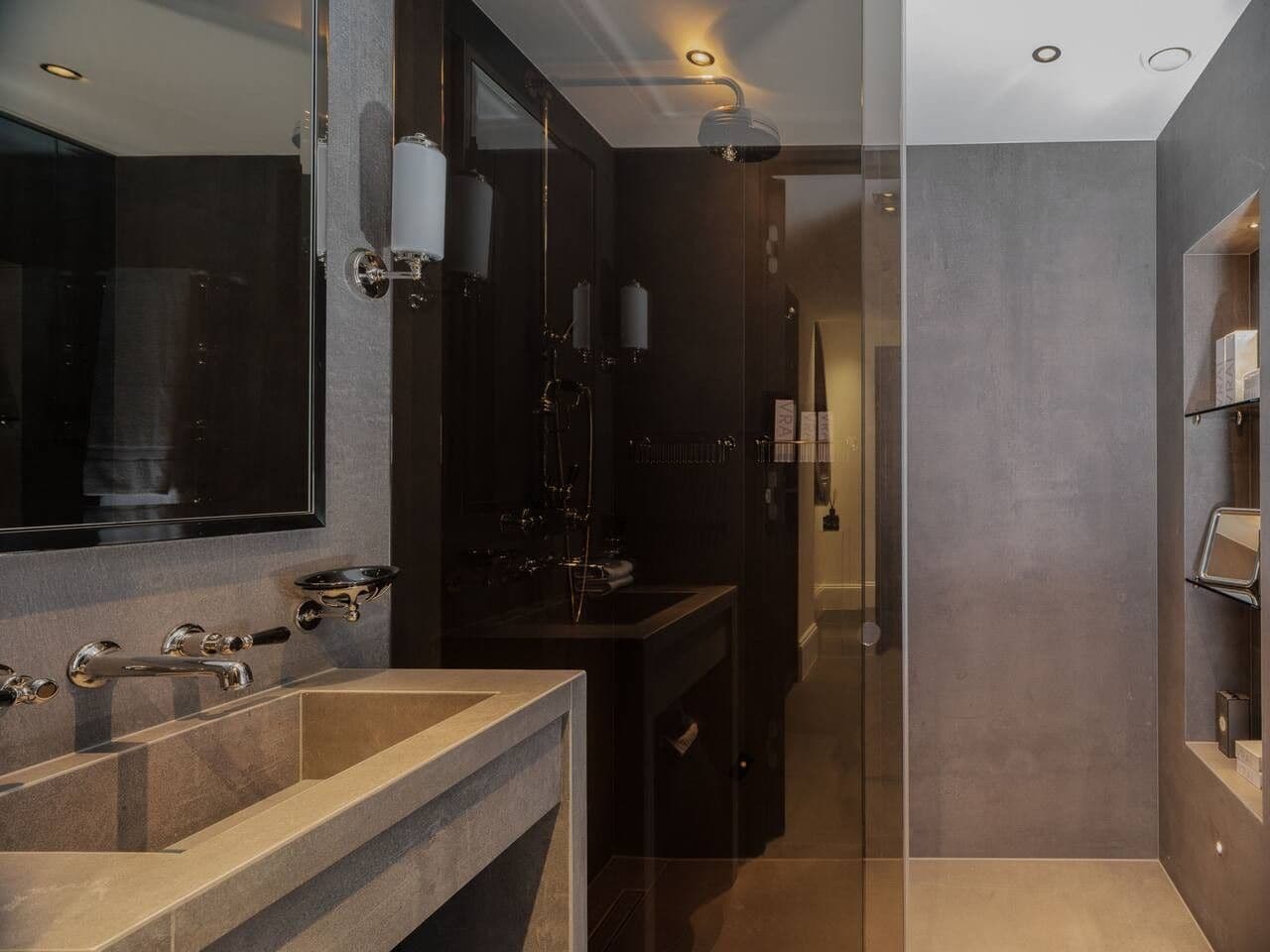 A modern bathroom with a large mirror, two sinks, and a shower area.
