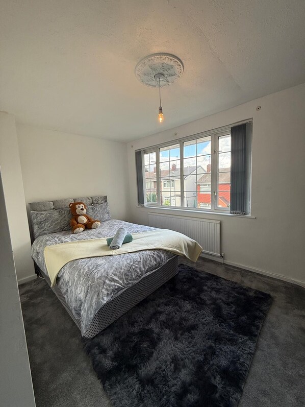 Ein Schlafzimmer mit einem Bett, einem Teddybären, einem Fenster und einer Heizung.