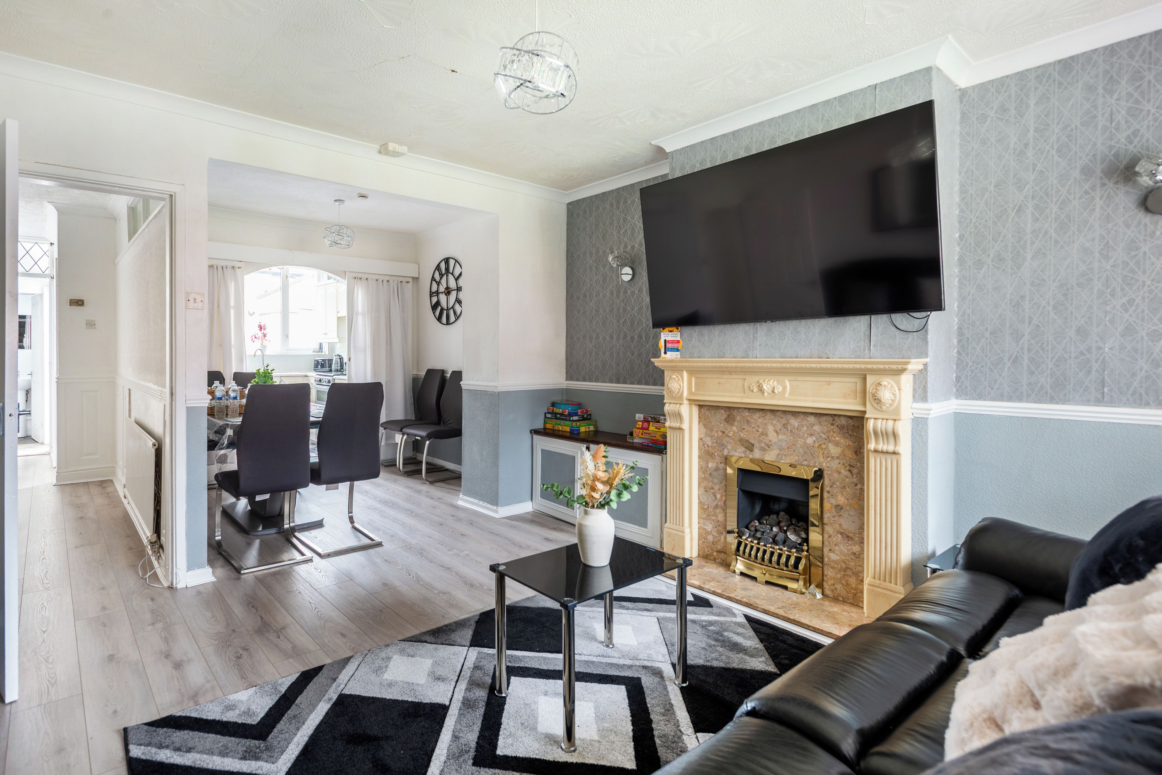 A modern living room with a fireplace, a dining area, and a kitchen in the background.