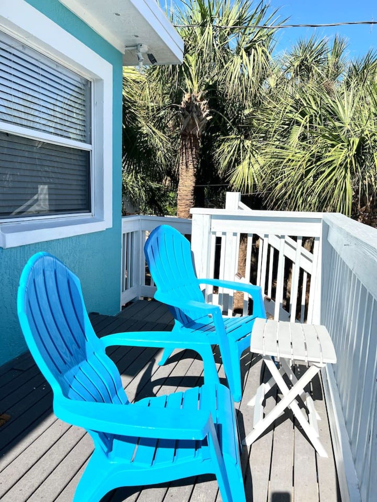 Una terraza de madera con dos sillas Adirondack turquesas y una mesita.