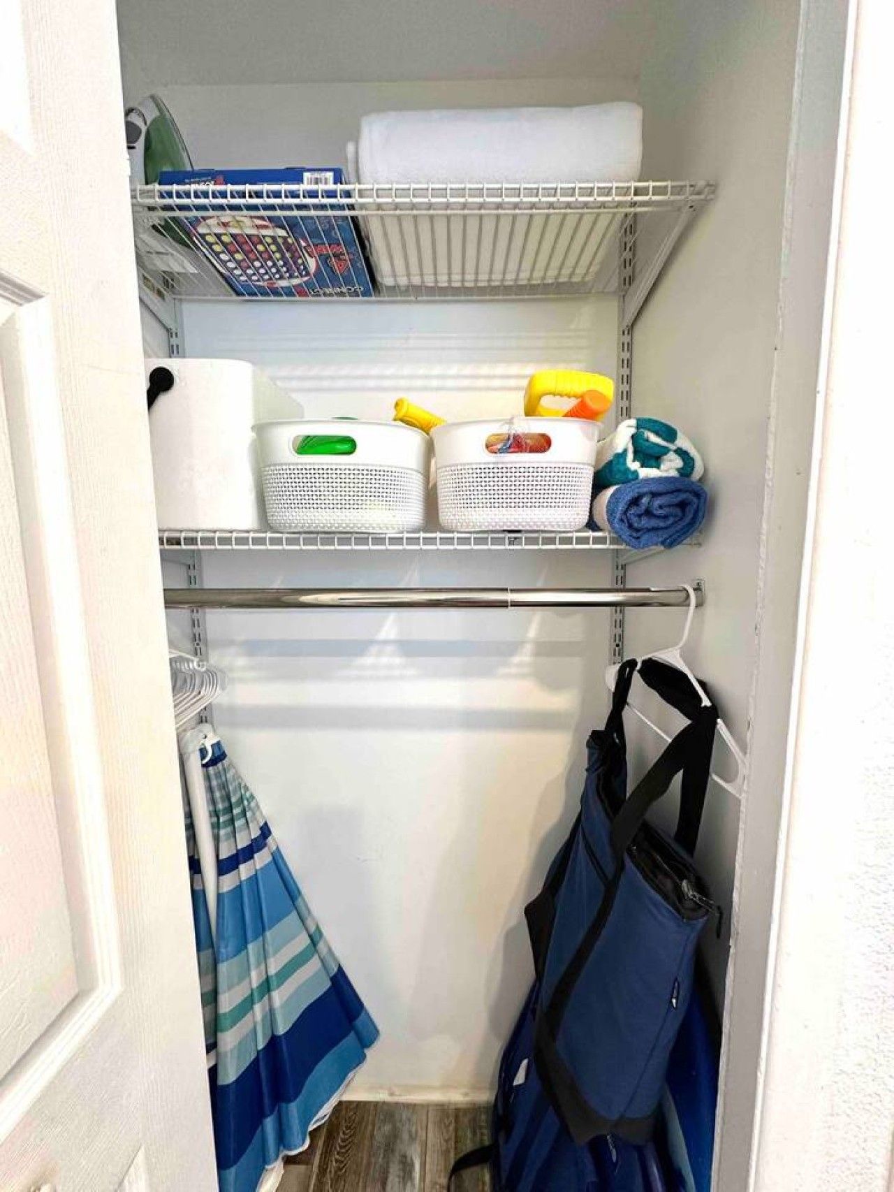 A storage closet with shelves containing various items like baskets, a rolled-up towel, and a blue bag.