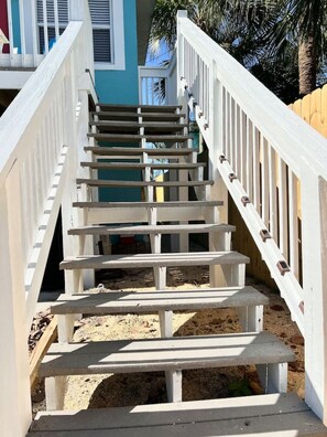 Eine Holztreppe mit weißen Geländern führt zu einem Gebäude mit blauer Fassade.
