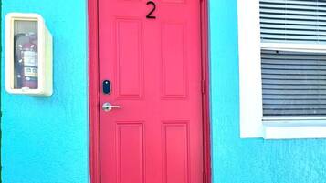 Una puerta roja con el número 2, un buzón y un felpudo sobre una terraza de madera.