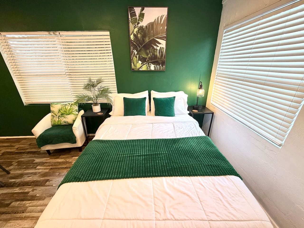 Un dormitorio con cama, una silla, mesita de noche, lámpara y ventana con persianas.