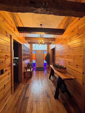 Un interior de madera con un pasillo central, un candelabro y una puerta con ventanal.
