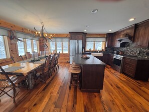 A spacious kitchen with wooden flooring, a central island, and a dining area with a large wooden table and chairs. - Secluded 5-BR Wooded Cabin Retreat with Panoramic Views in Vanderbilt (Vanderbilt)