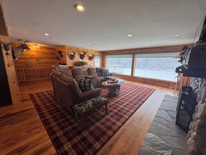 A cozy cabin interior with a wooden floor, a sofa, a coffee table, and a fireplace with mounted animal heads. - Secluded 5-BR Wooded Cabin Retreat with Panoramic Views in Vanderbilt (Vanderbilt)