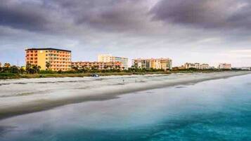 Un hotel frente a la playa con varias construcciones, una playa de arena y aguas tranquilas.