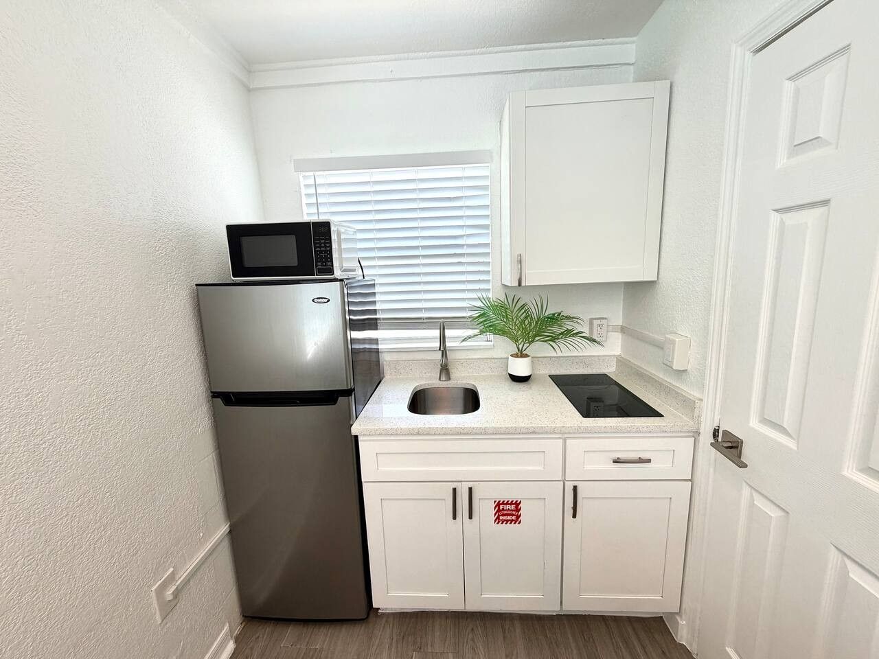Una cocina compacta con refrigerador, microondas, lavamanos y armarios.