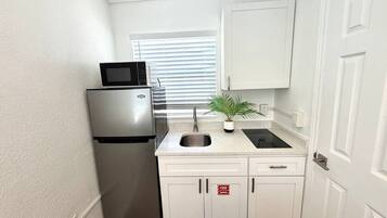 Una cocina compacta con refrigerador, microondas, lavamanos y armarios.