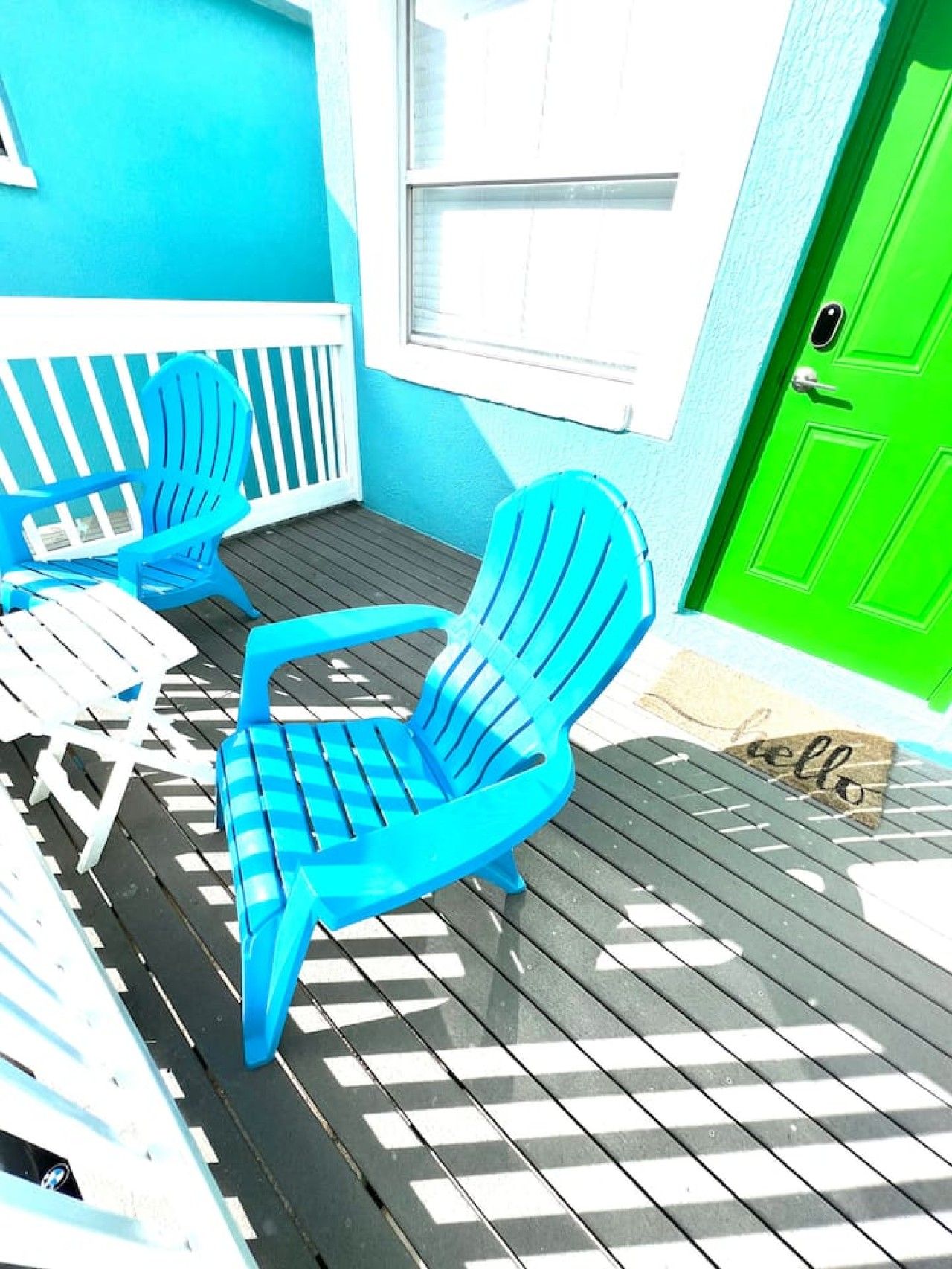 Una terraza con dos sillas Adirondack azules, una mesa blanca y una puerta verde.