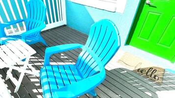 Una terraza con dos sillas Adirondack azules, una mesa blanca y una puerta verde.