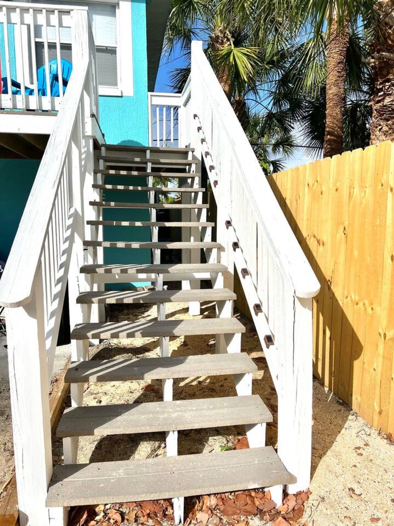 Una escalera de madera con barandillas blancas que conduce a un edificio azul.