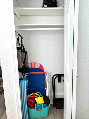 Un placard de rangement avec des étagères, un sac suspendu et divers objets, notamment une valise bleue et un panier à rayures.