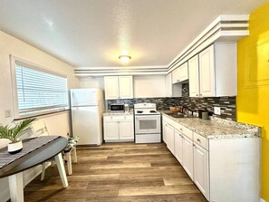 A compact kitchen with white cabinets, a microwave, stove, and a refrigerator. - 1 bdrm:beach across st, Port  8 mi, Ron Jon’s 4 mi (Cocoa Beach)