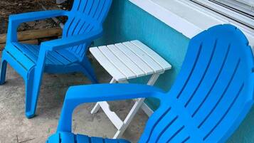 Dos sillas Adirondack azules y una mesita blanca frente a un edificio con una ventana.