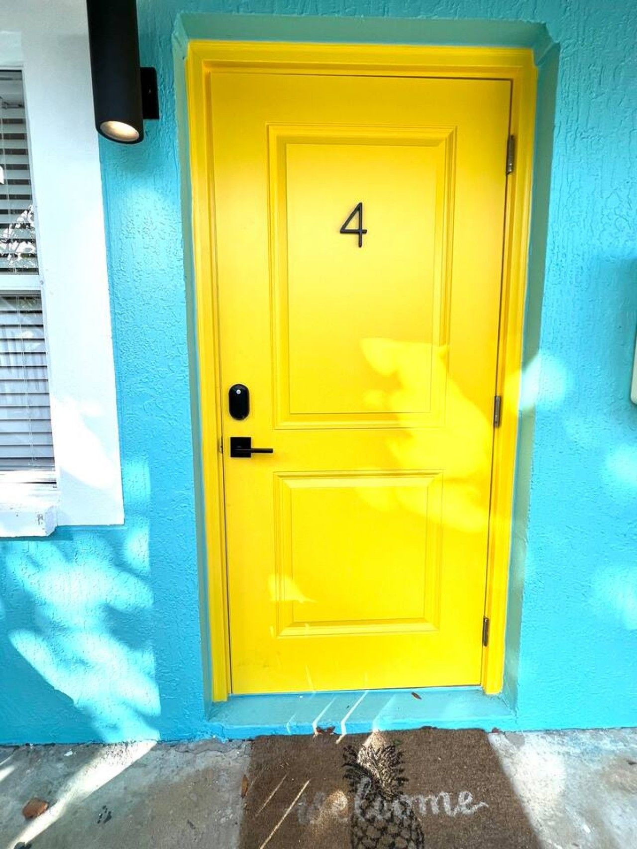 A yellow door with the number 4, a doormat with 'welcome' written on it, and a blue wall.