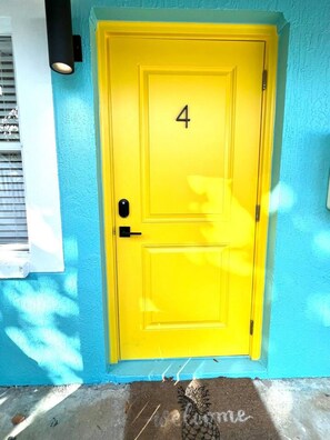 A yellow door with the number 4, a doormat with 'welcome' written on it, and a blue wall. - 1 bdrm:beach across st, Port  8 mi, Ron Jon’s 4 mi (Cocoa Beach)