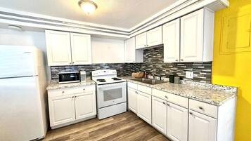 Una cocina con armarios blancos, microondas, estufa y salpicadero de azulejos.